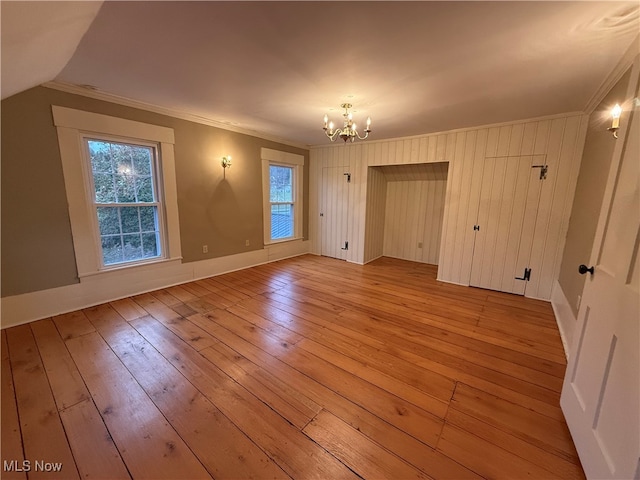 empty room with an inviting chandelier, light hardwood / wood-style floors, and crown molding