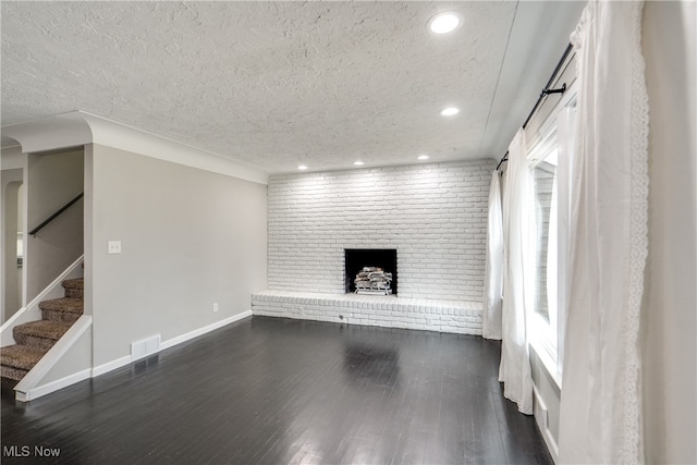 unfurnished living room with brick wall, a brick fireplace, dark wood-type flooring, and a textured ceiling