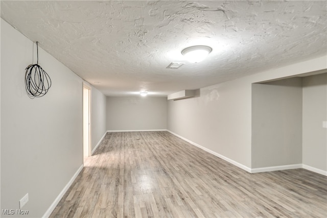 basement with hardwood / wood-style flooring, a wall mounted AC, and a textured ceiling