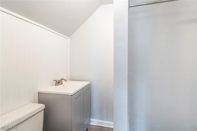 bathroom featuring vanity, hardwood / wood-style floors, vaulted ceiling, and toilet