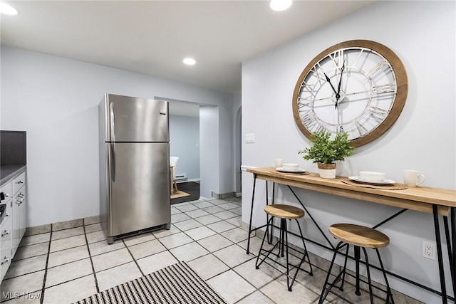 kitchen featuring a breakfast bar, light tile patterned floors, white cabinets, and stainless steel refrigerator