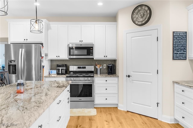 kitchen with white cabinets, pendant lighting, appliances with stainless steel finishes, tasteful backsplash, and light hardwood / wood-style floors