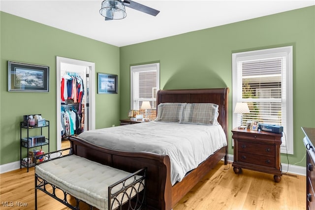 bedroom with a closet, a spacious closet, light hardwood / wood-style floors, and multiple windows