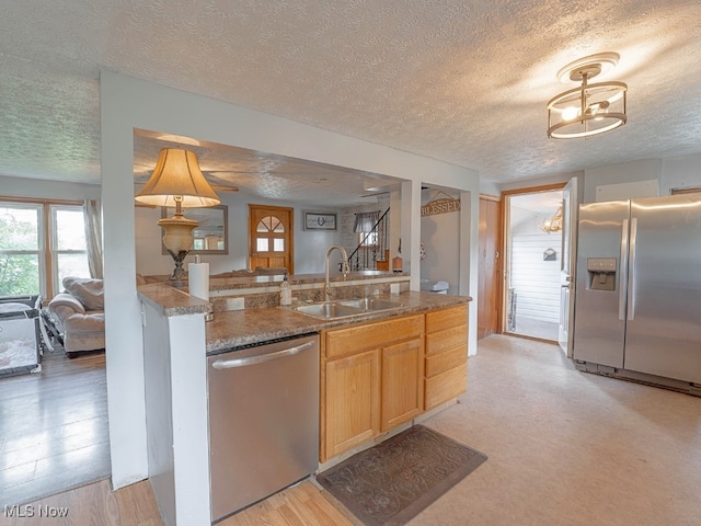 kitchen with appliances with stainless steel finishes, a textured ceiling, light hardwood / wood-style flooring, and sink