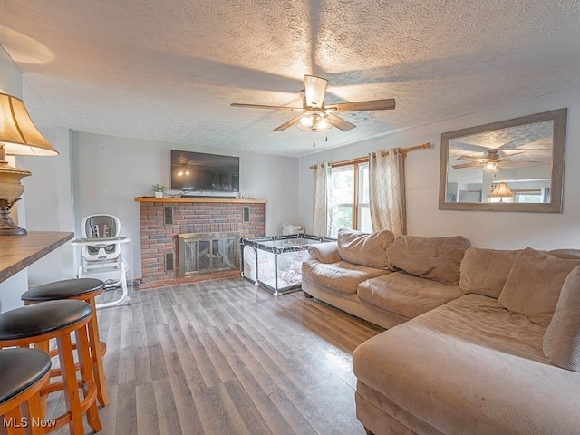 living room featuring a fireplace, ceiling fan, hardwood / wood-style floors, and a textured ceiling