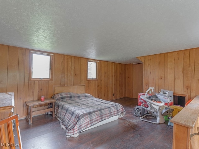 bedroom with a textured ceiling, dark hardwood / wood-style floors, multiple windows, and wooden walls