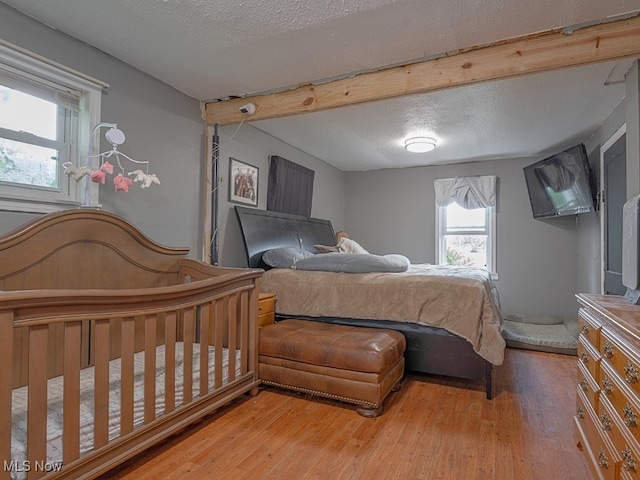 bedroom featuring hardwood / wood-style floors, beamed ceiling, and a textured ceiling