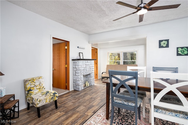 dining room featuring ceiling fan, a fireplace, wood-type flooring, and a textured ceiling