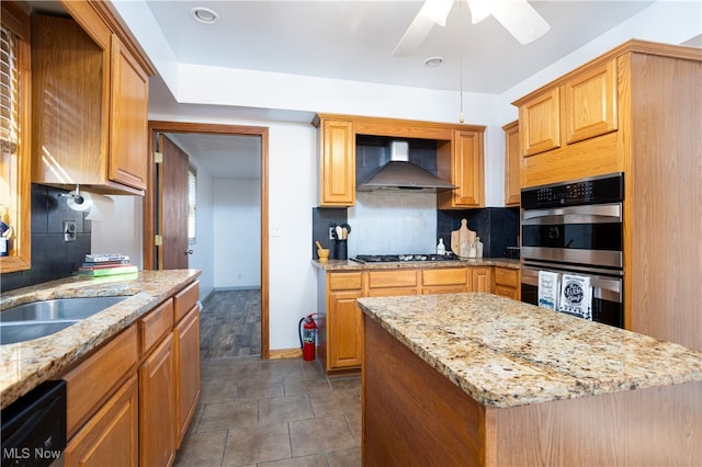 kitchen featuring wall chimney exhaust hood, a center island, light stone countertops, and double oven