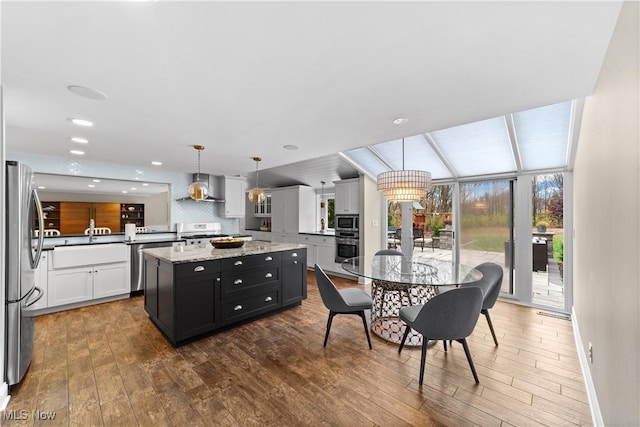 kitchen with a kitchen island, white cabinets, hanging light fixtures, stainless steel appliances, and wall chimney exhaust hood