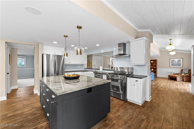 kitchen with wall chimney exhaust hood, lofted ceiling, white cabinetry, hanging light fixtures, and stainless steel appliances