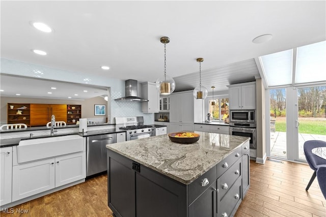 kitchen with wall chimney exhaust hood, white cabinetry, decorative light fixtures, appliances with stainless steel finishes, and a kitchen island