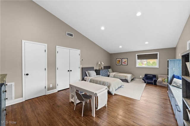 bedroom with dark hardwood / wood-style flooring, high vaulted ceiling, and multiple closets