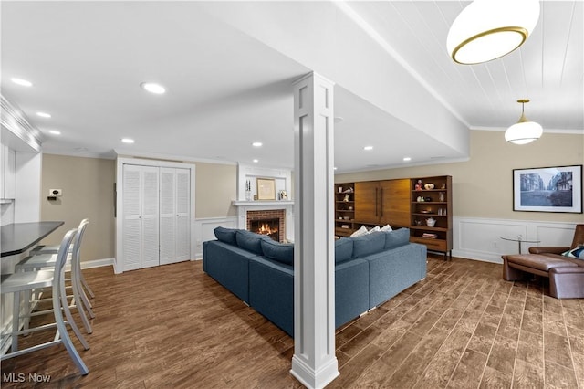 living room with dark wood-type flooring, ornamental molding, and a brick fireplace