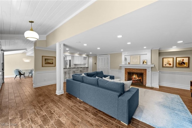 living room featuring ornate columns, ornamental molding, a brick fireplace, and dark hardwood / wood-style floors