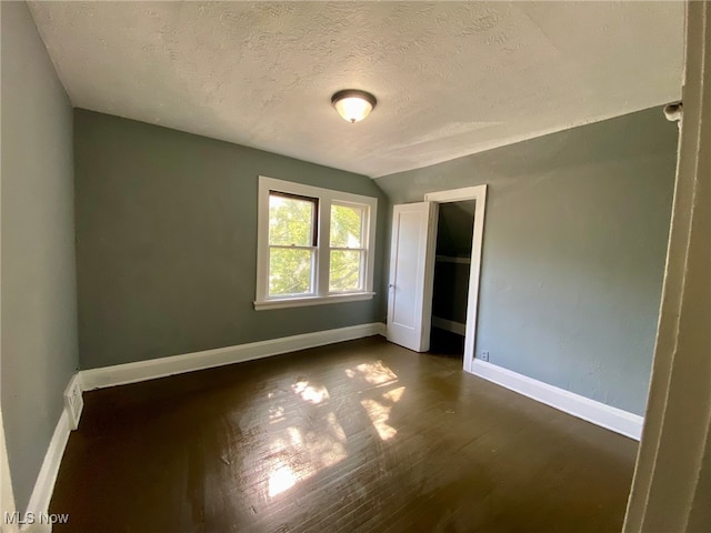 unfurnished bedroom with dark wood-type flooring, vaulted ceiling, and a textured ceiling