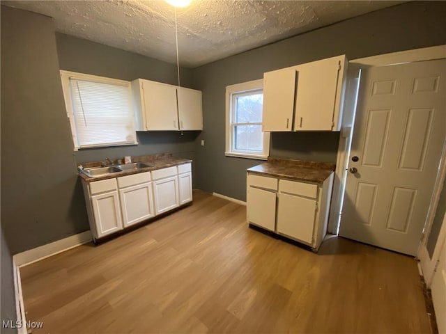 kitchen with white cabinetry, sink, a textured ceiling, and light wood-type flooring