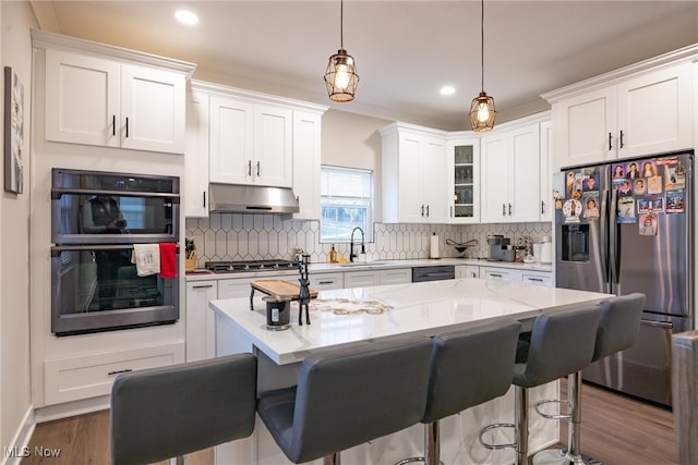 kitchen featuring white cabinets, a center island, stainless steel appliances, and hanging light fixtures