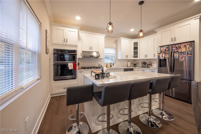 kitchen featuring white cabinetry, decorative backsplash, hanging light fixtures, dark wood-type flooring, and stainless steel appliances