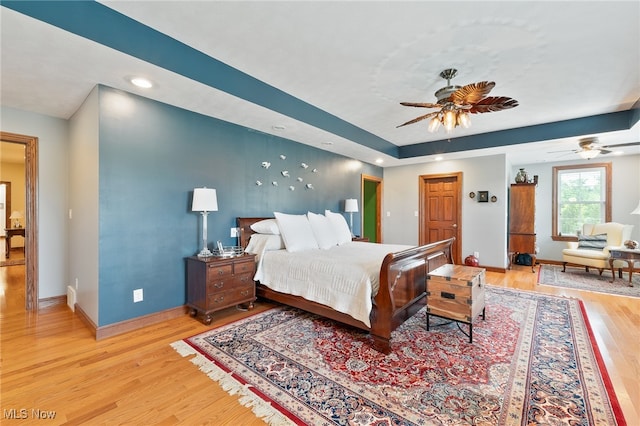 bedroom featuring a raised ceiling, light hardwood / wood-style flooring, and ceiling fan