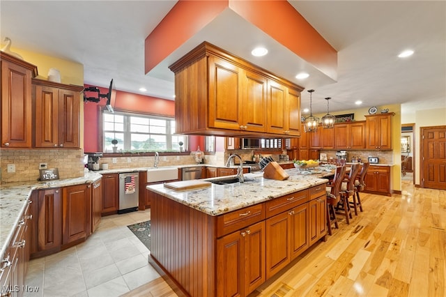 kitchen featuring light hardwood / wood-style flooring, sink, an island with sink, decorative light fixtures, and light stone countertops