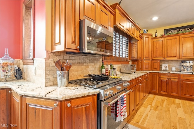 kitchen with light hardwood / wood-style flooring, light stone counters, stainless steel appliances, and tasteful backsplash