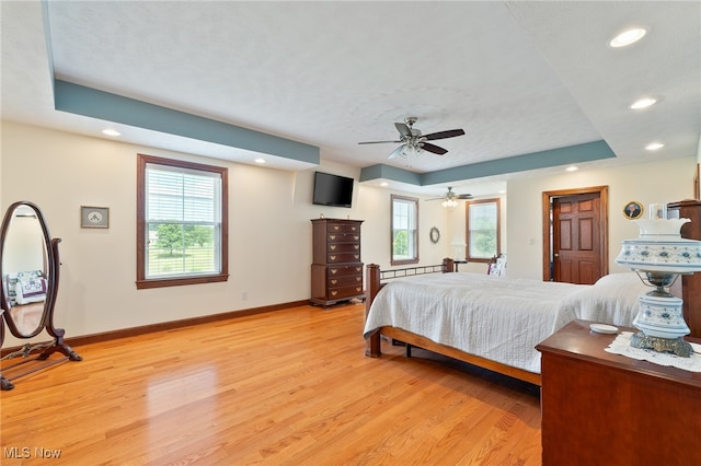 bedroom with a baseboard heating unit, ceiling fan, a raised ceiling, and light wood-type flooring