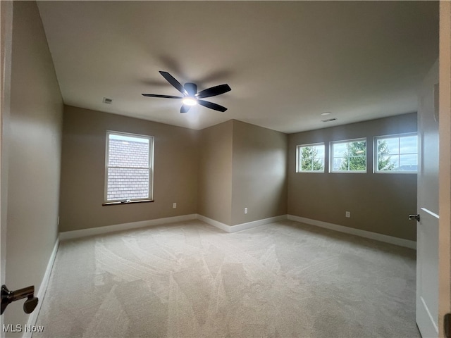 spare room featuring light colored carpet, a wealth of natural light, and ceiling fan