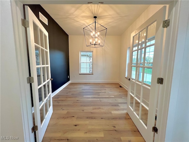 unfurnished dining area with a wealth of natural light, a notable chandelier, light hardwood / wood-style floors, and french doors