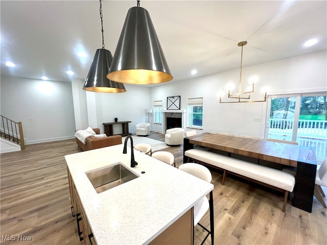 kitchen with sink, a center island with sink, light hardwood / wood-style floors, decorative light fixtures, and light stone counters