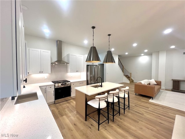 kitchen featuring appliances with stainless steel finishes, light wood-type flooring, a breakfast bar, wall chimney range hood, and white cabinets