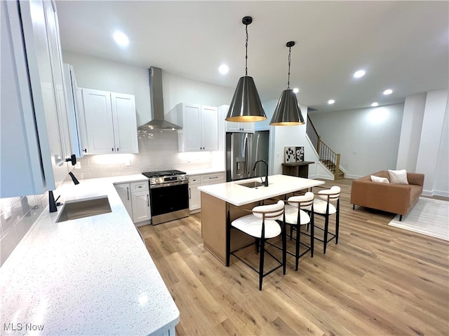 kitchen with white cabinetry, wall chimney exhaust hood, an island with sink, and appliances with stainless steel finishes