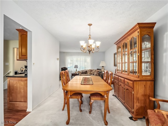 dining area featuring a textured ceiling, light carpet, and a chandelier