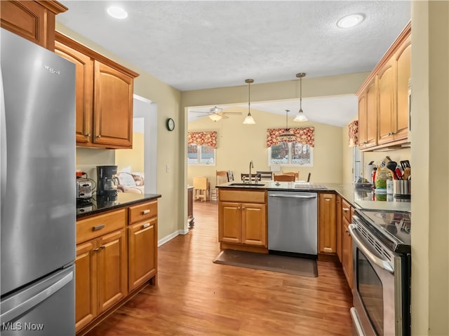 kitchen featuring kitchen peninsula, stainless steel appliances, sink, wood-type flooring, and pendant lighting