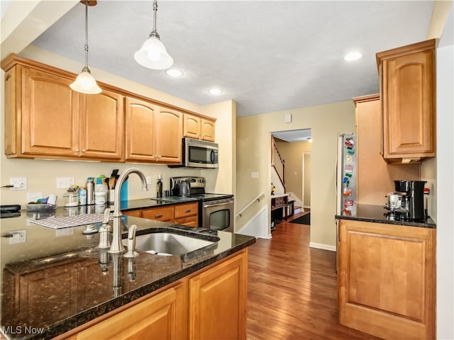 kitchen with sink, hanging light fixtures, dark hardwood / wood-style floors, dark stone countertops, and appliances with stainless steel finishes