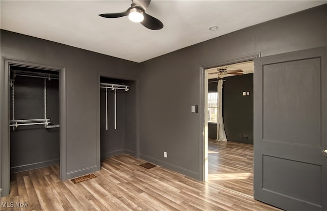 unfurnished bedroom with ceiling fan, light wood-type flooring, and two closets