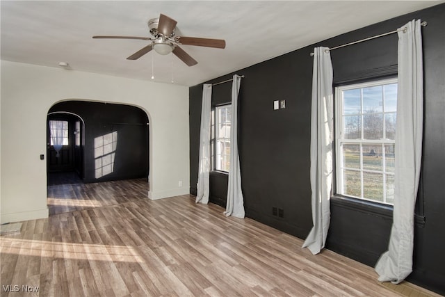 empty room with ceiling fan, plenty of natural light, and light hardwood / wood-style flooring