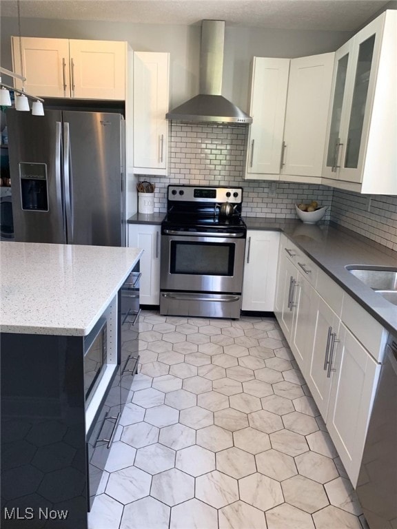 kitchen featuring white cabinets, wall chimney exhaust hood, stainless steel appliances, and tasteful backsplash