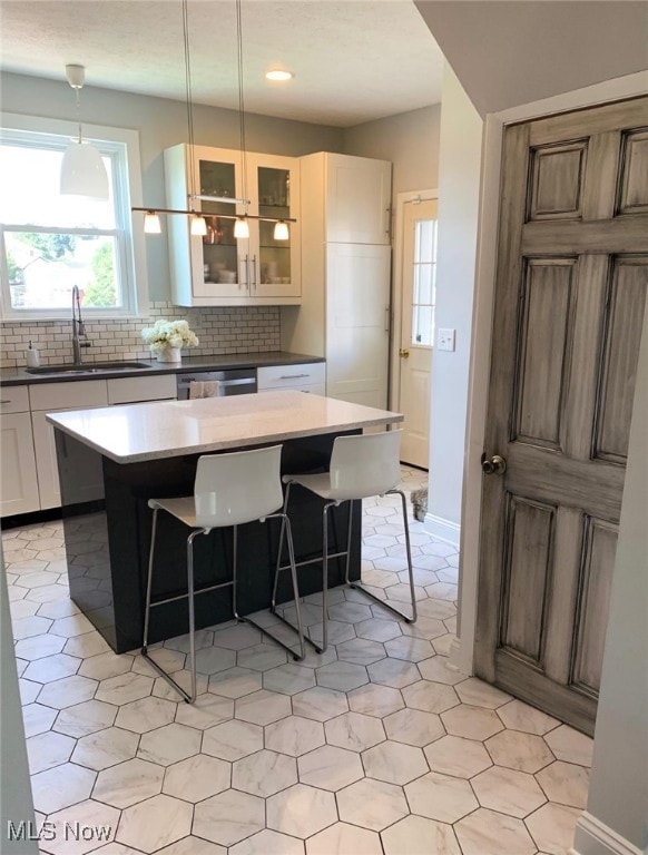 kitchen featuring white cabinets, a center island, sink, and hanging light fixtures