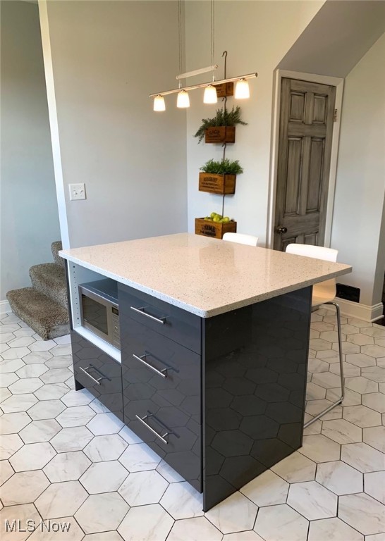 kitchen featuring light stone countertops, a kitchen breakfast bar, gray cabinetry, pendant lighting, and a center island