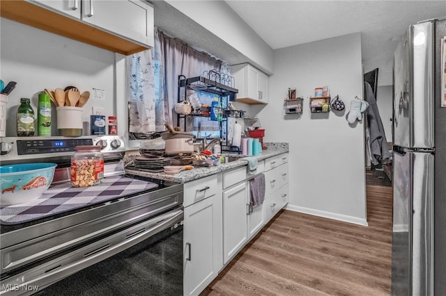 kitchen with hardwood / wood-style floors, sink, white cabinets, light stone counters, and stainless steel appliances