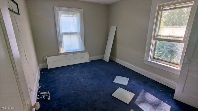 empty room with radiator heating unit, dark carpet, and plenty of natural light