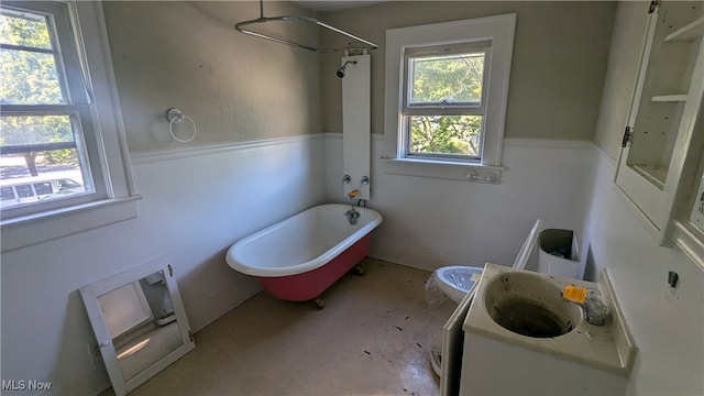 bathroom featuring concrete floors, a tub to relax in, a healthy amount of sunlight, and sink