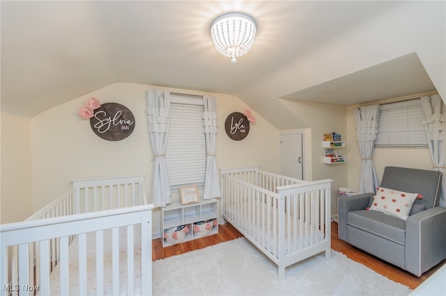 bedroom featuring lofted ceiling, wood-type flooring, and a crib