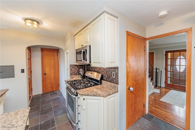 kitchen featuring backsplash, white cabinets, dark hardwood / wood-style floors, appliances with stainless steel finishes, and light stone counters