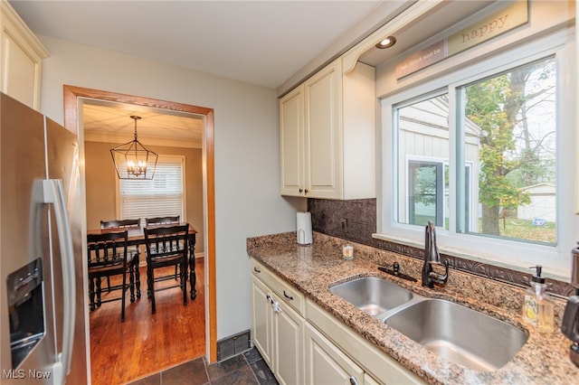 kitchen with sink, stainless steel refrigerator with ice dispenser, decorative light fixtures, light stone counters, and a chandelier