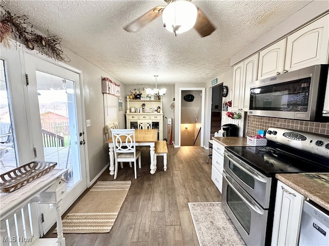 kitchen featuring backsplash, appliances with stainless steel finishes, decorative light fixtures, white cabinets, and hardwood / wood-style flooring