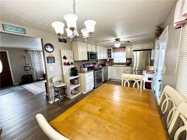 kitchen with dark wood-type flooring, hanging light fixtures, stainless steel appliances, tasteful backsplash, and ceiling fan with notable chandelier