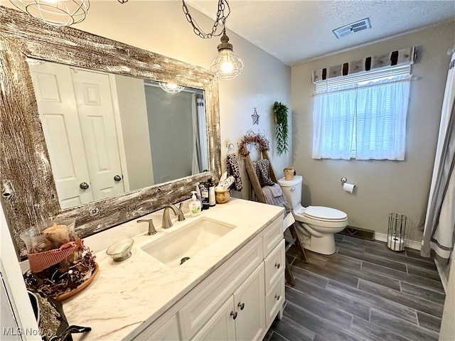 bathroom featuring a textured ceiling, vanity, hardwood / wood-style flooring, and toilet