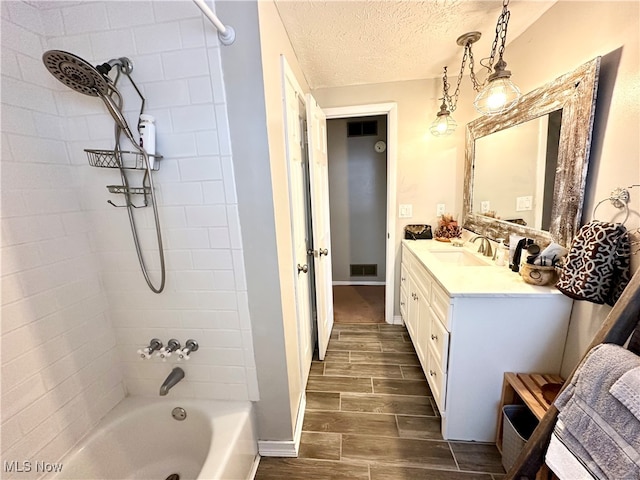 bathroom with vanity, a textured ceiling, and tiled shower / bath